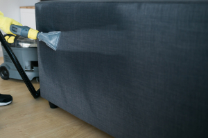 Cleaning service company employee removing dirt from furniture in flat with professional equipment. Man arm cleaning sofa with washing vacuum cleaner close up copy space
