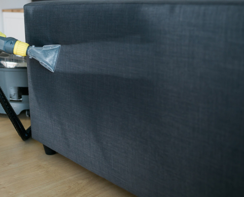 Cleaning service company employee removing dirt from furniture in flat with professional equipment. Man arm cleaning sofa with washing vacuum cleaner close up copy space